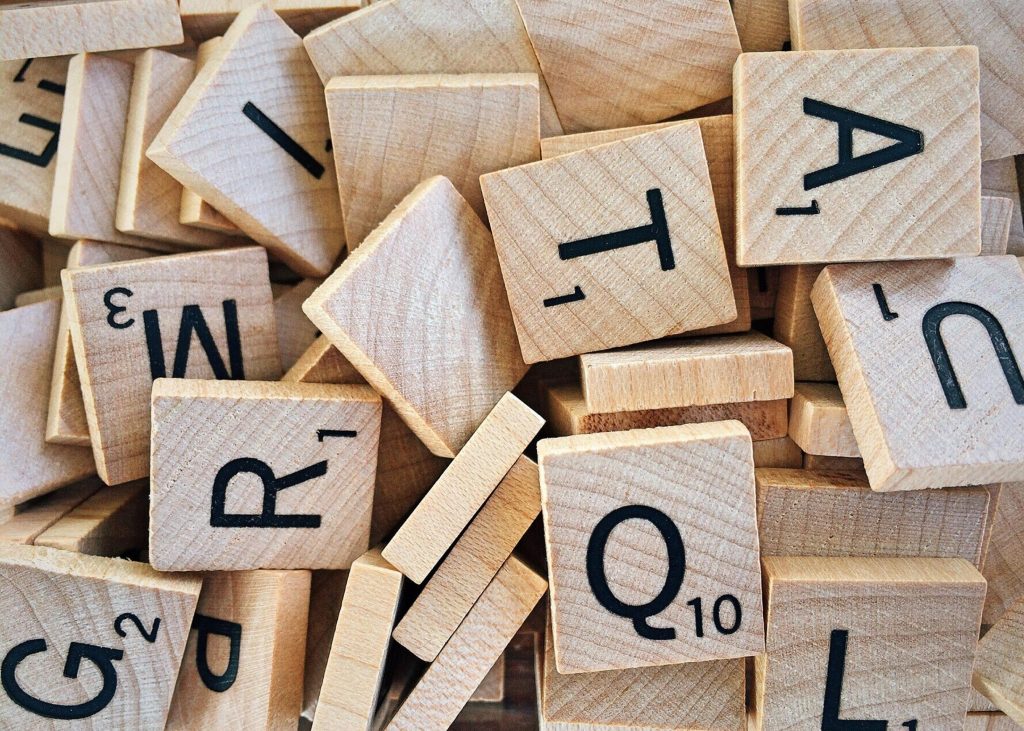 Pile of wooden Scrabble tiles displaying various letters and numbers.